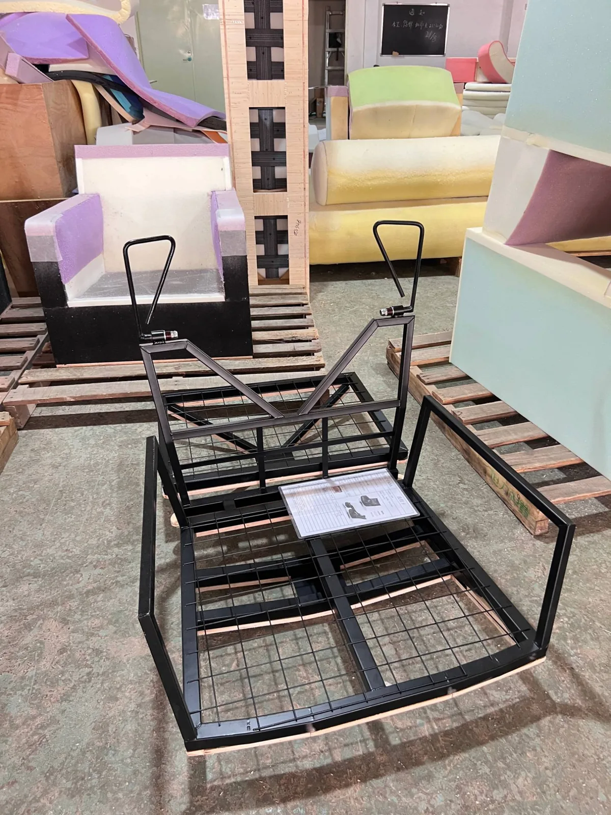 Black powder-coated steel chair frame with mesh seat panel and the order spec card resting on it, foam blocks behind