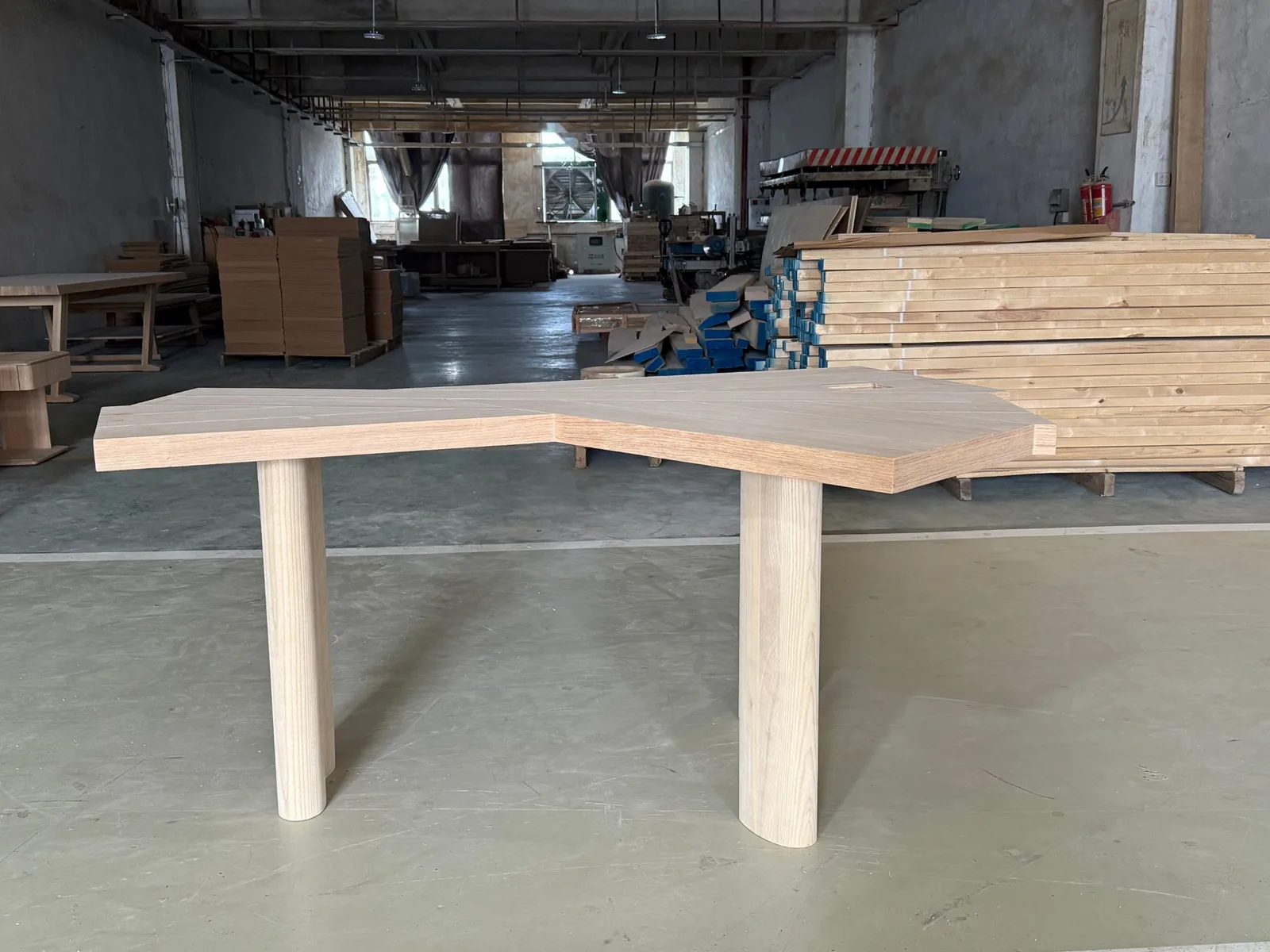 Custom angled oak desk with two round column legs standing on the workshop floor of a Foshan solid-timber factory
