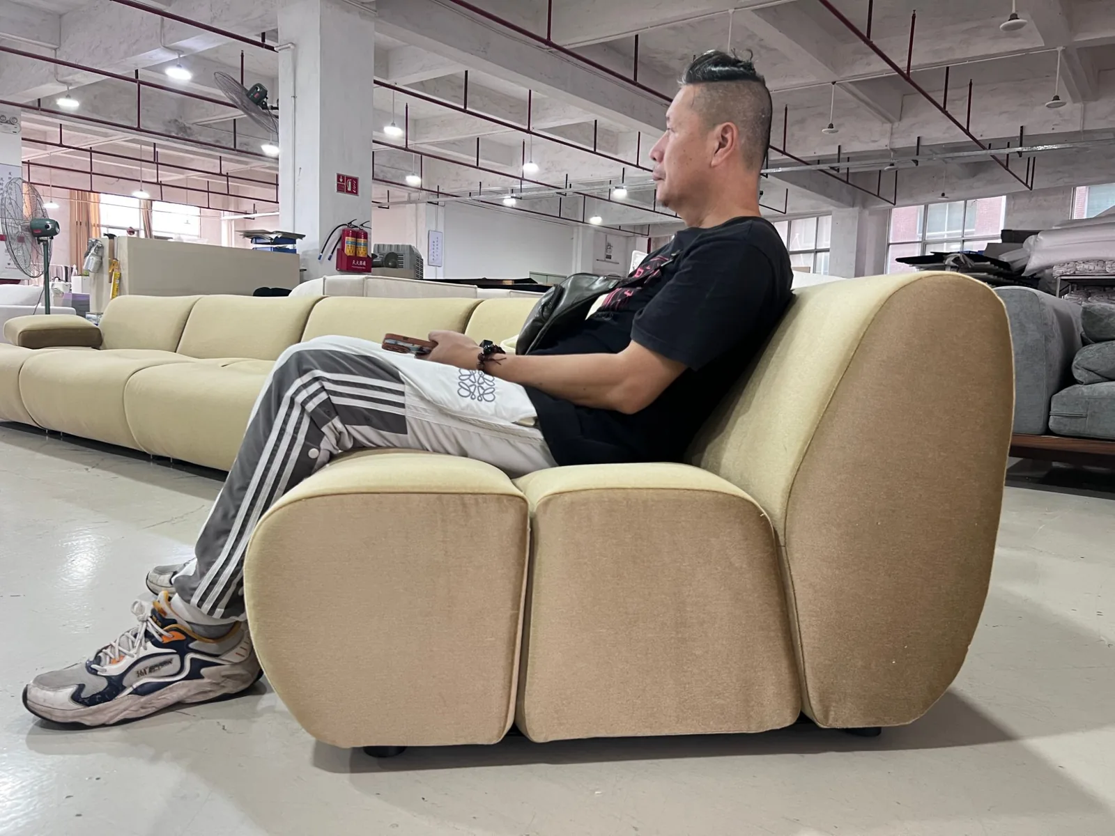 Source Foshan inspector sitting in a camel-coloured curved lounge chair in a Longjiang sofa factory to test seat height and back angle
