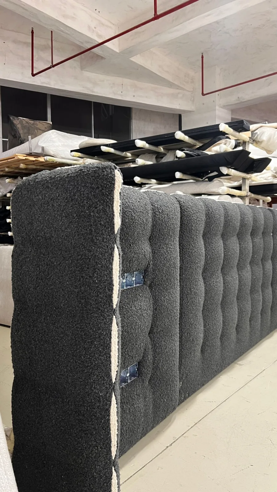 Charcoal boucle tufted hotel headboard with integrated power outlets, waiting in the upholstery workshop