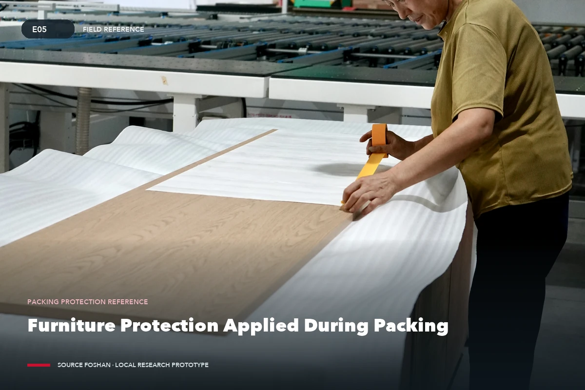 Worker applying protective material to a furniture component in a factory.