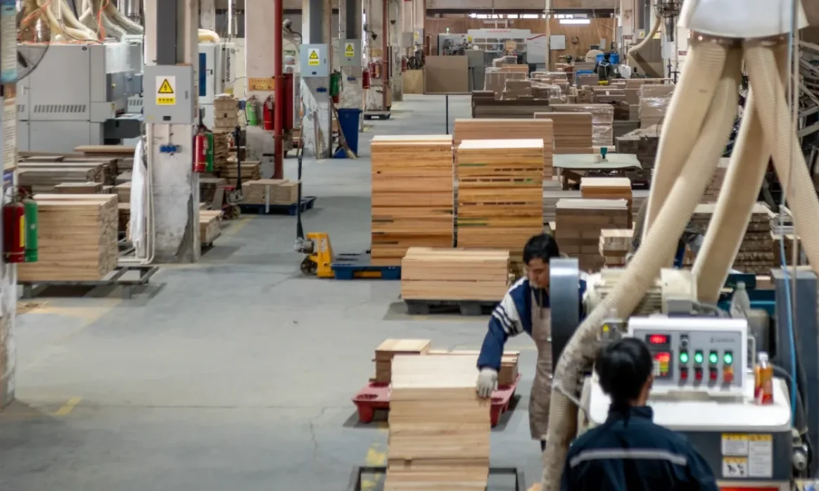 Solid-wood furniture factory floor in Foshan with stacked timber blanks and workers at the machines