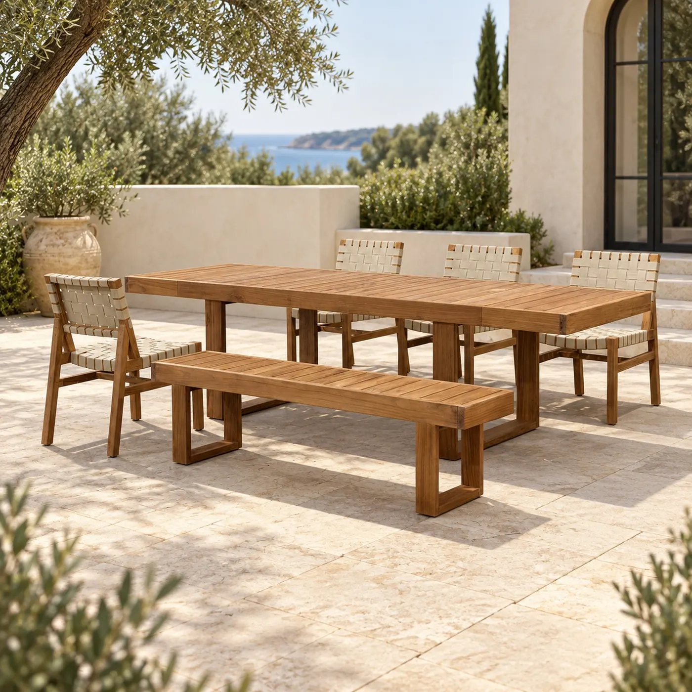 Long teak outdoor dining table with benches and rope chairs overlooking the sea