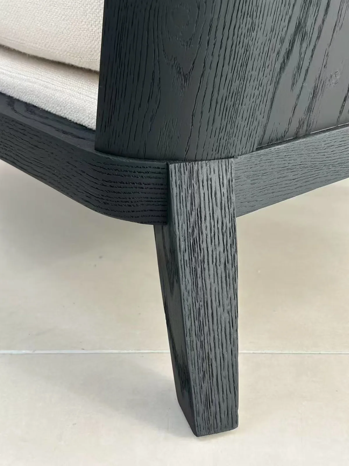 Black-stained oak sofa leg where it meets the curved rail, grain and joint visible