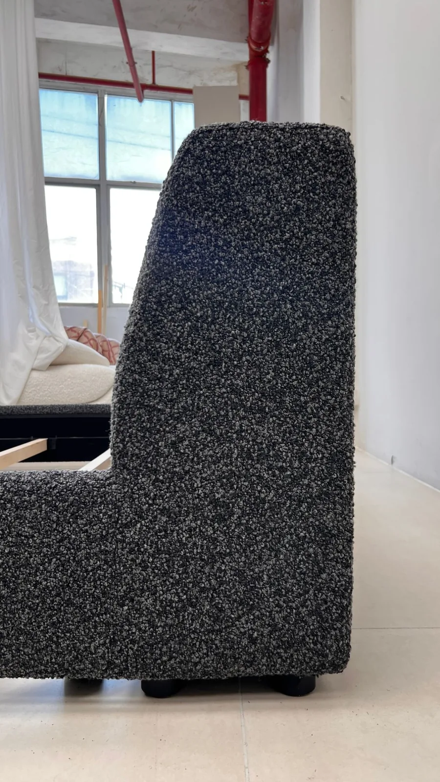 Side view of a charcoal boucle sofa with the timber frame of the next module visible behind