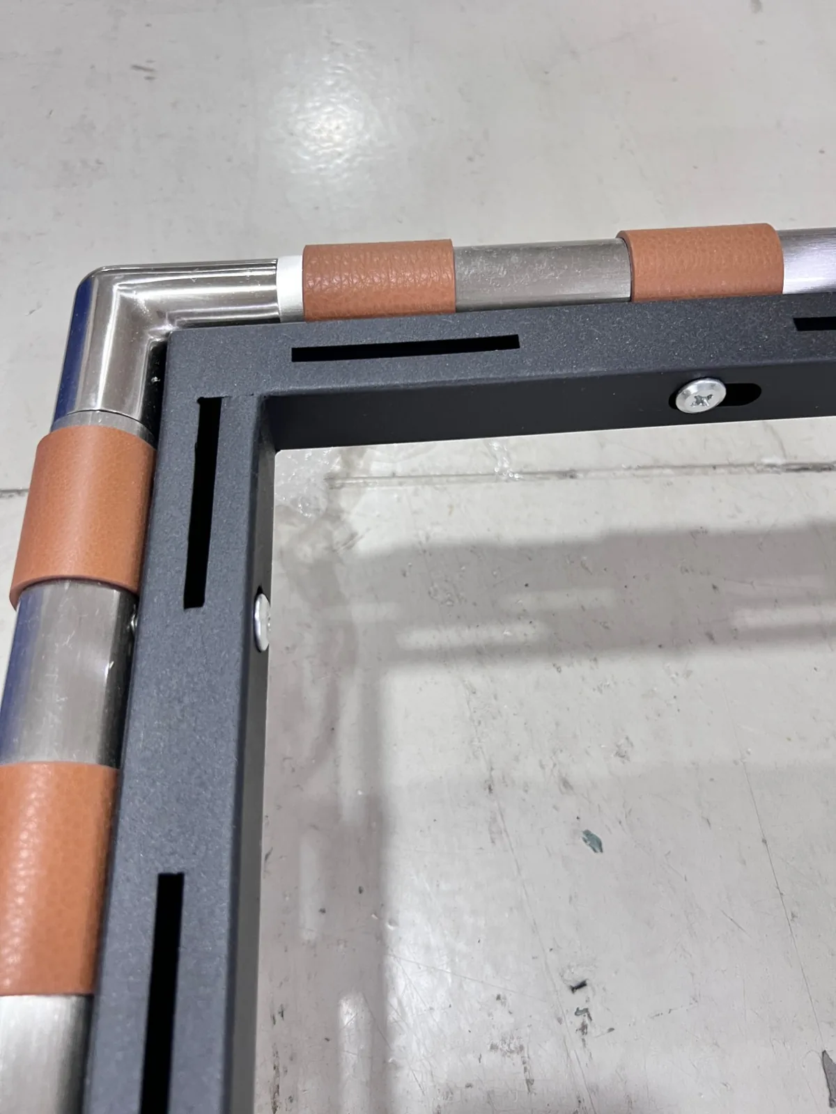 Corner of a powder-coated steel frame with stainless rail, leather sleeves and fixing screws
