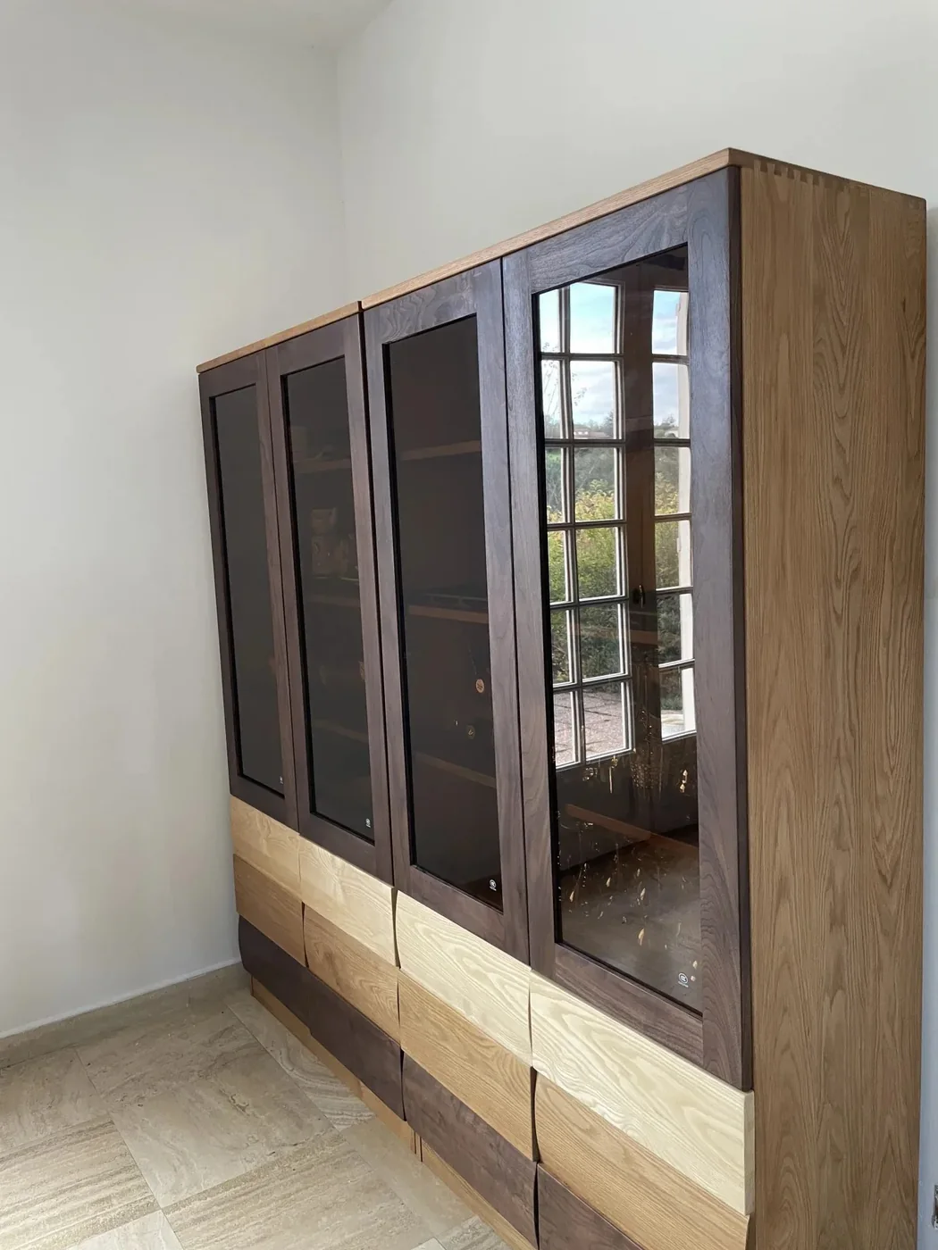 A solid-wood glazed display cabinet with patchwork drawer fronts installed in a French home