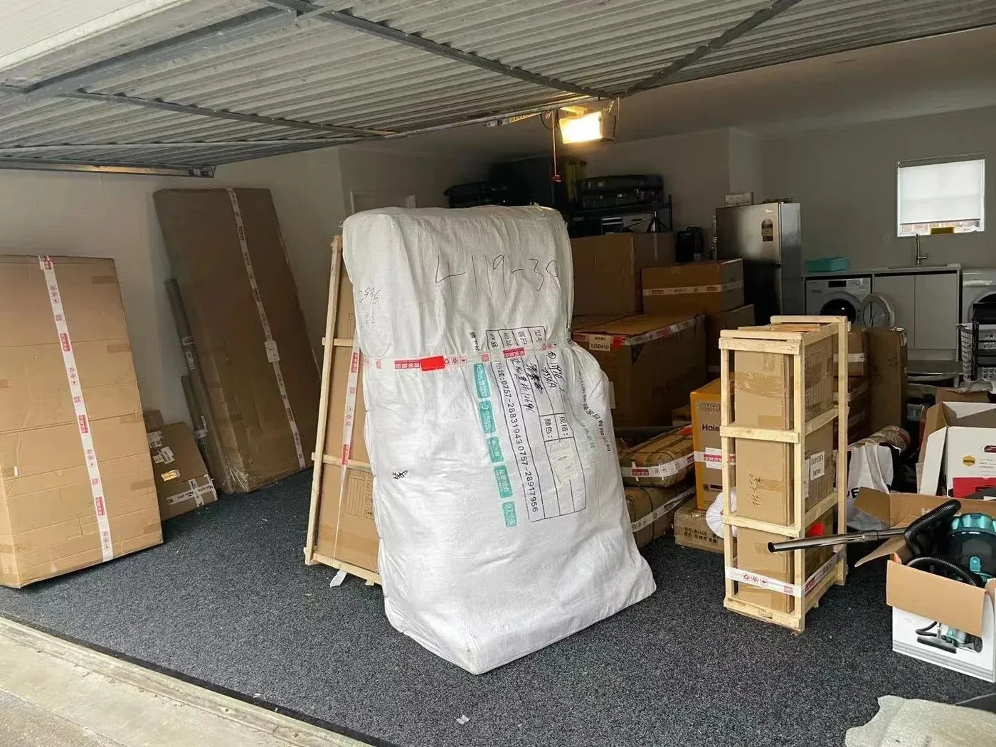 A New Zealand garage filled with cartons, a woven-bag-wrapped sofa and a timber crate on arrival day