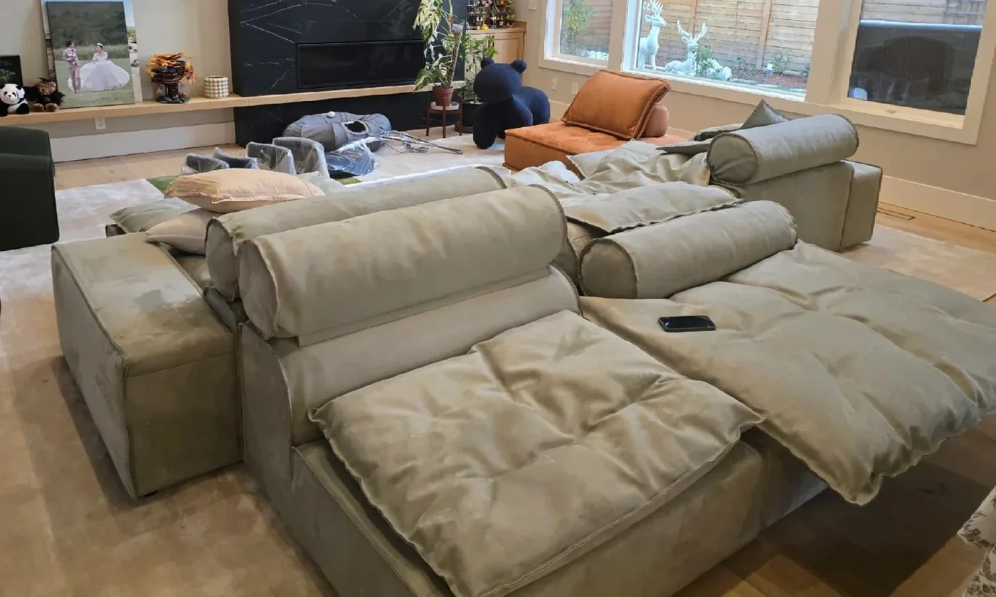 A sage-green modular sofa being unwrapped and assembled in a US living room, cushions still loose