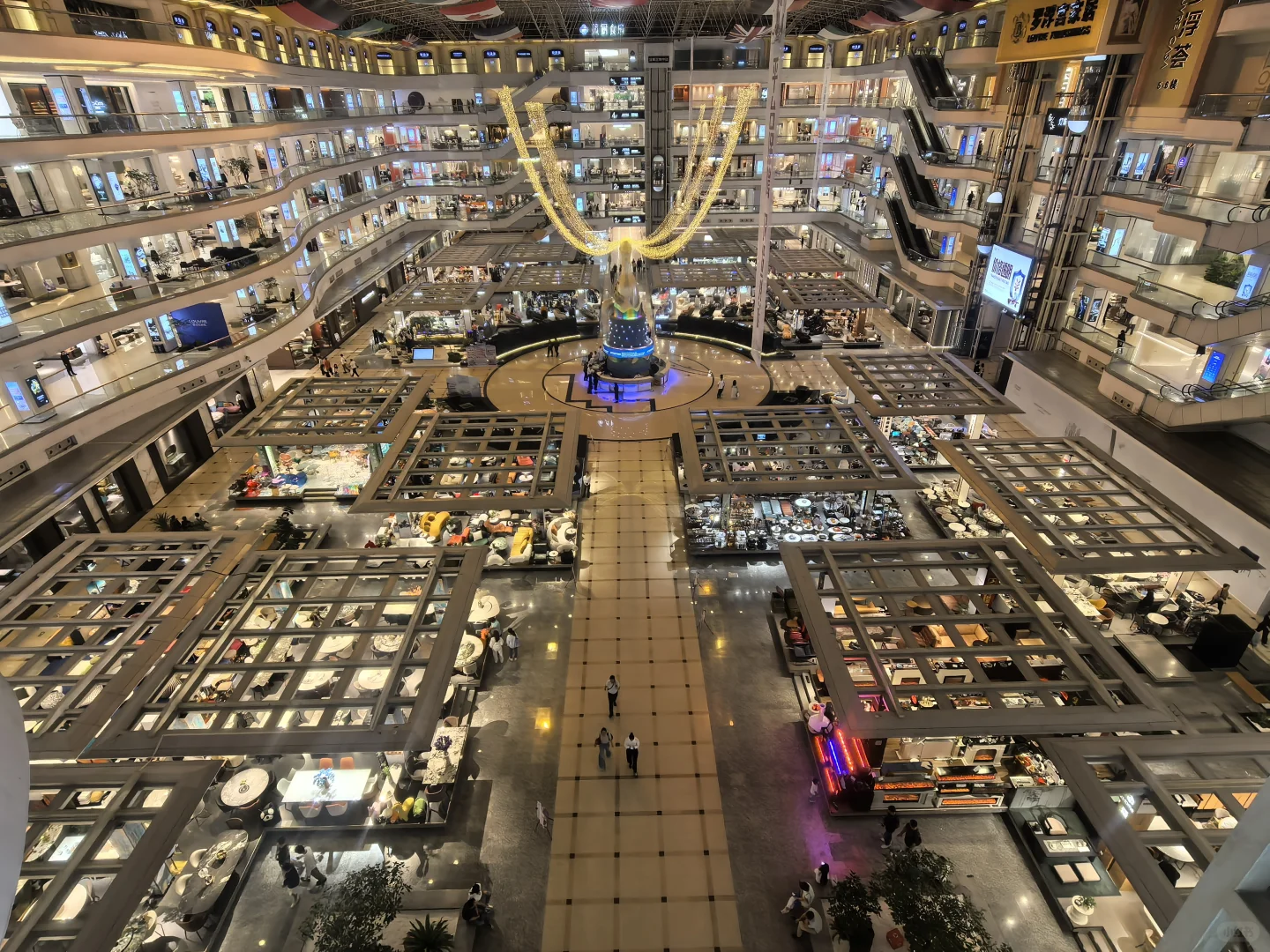 An elevated view of Louvre's multi-level shopping atrium, with escalators, display islands and a central bottle-shaped installation.