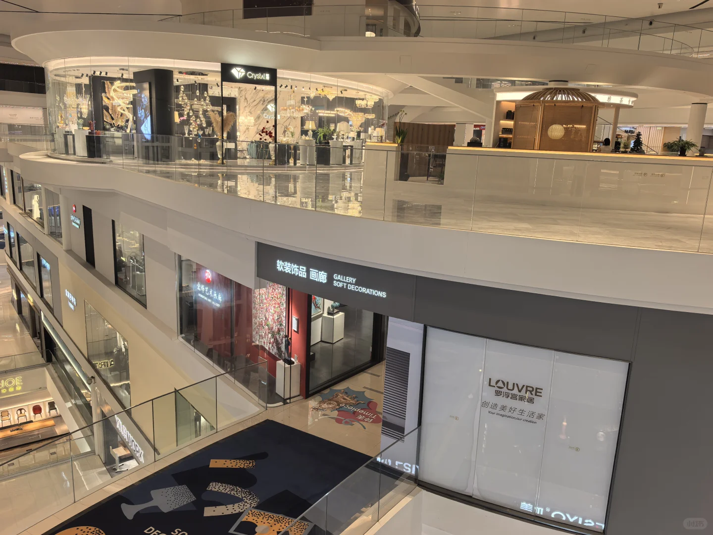 Curved white balconies and glass balustrades overlook a gallery entrance, with lighting displays on the level above.