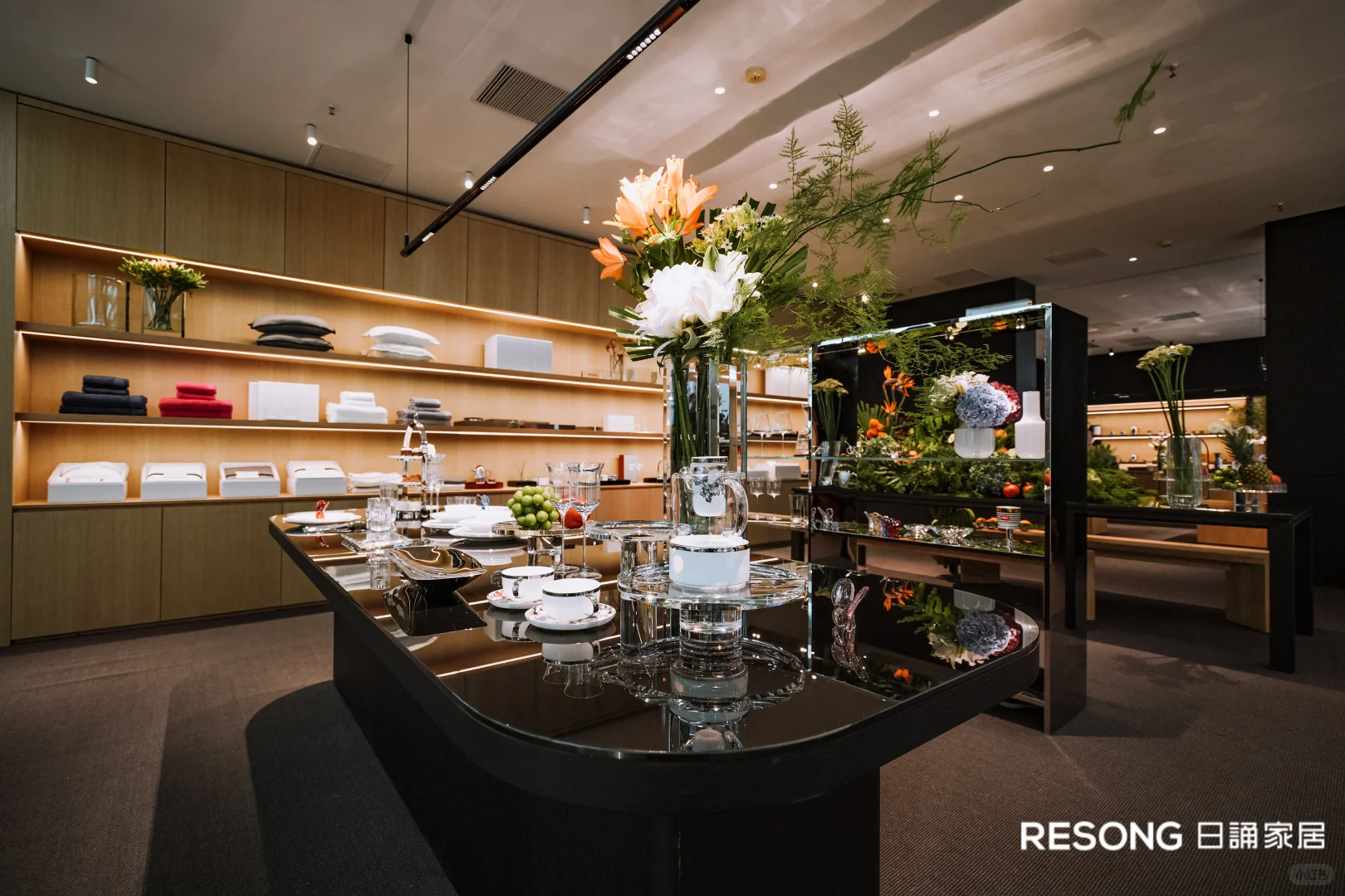Glassware, white tableware and tall flowers arranged on a black oval table inside the RESONG display.