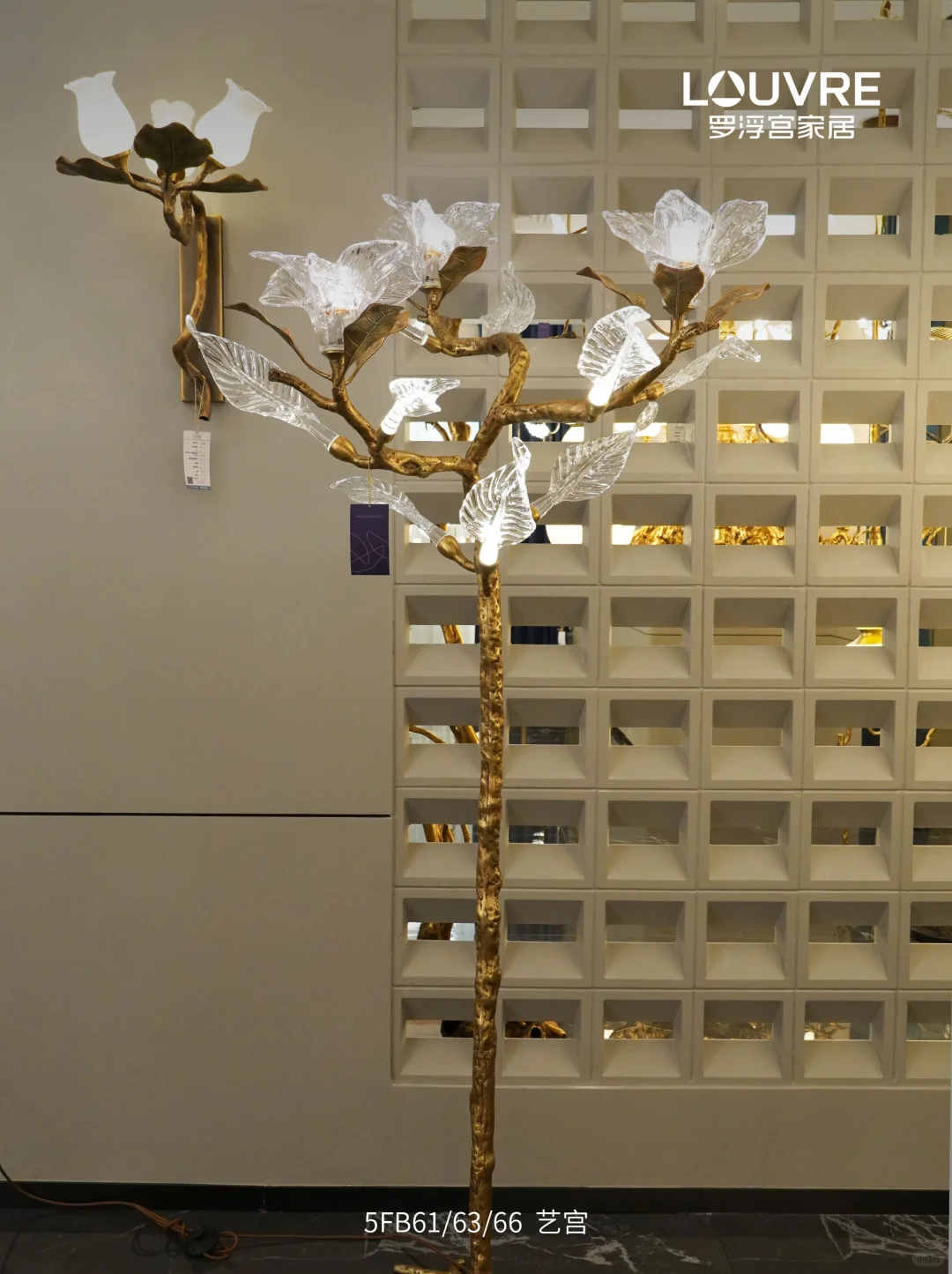 Branch-shaped gold-toned floor light with translucent leaf and flower shades against a pale geometric screen.