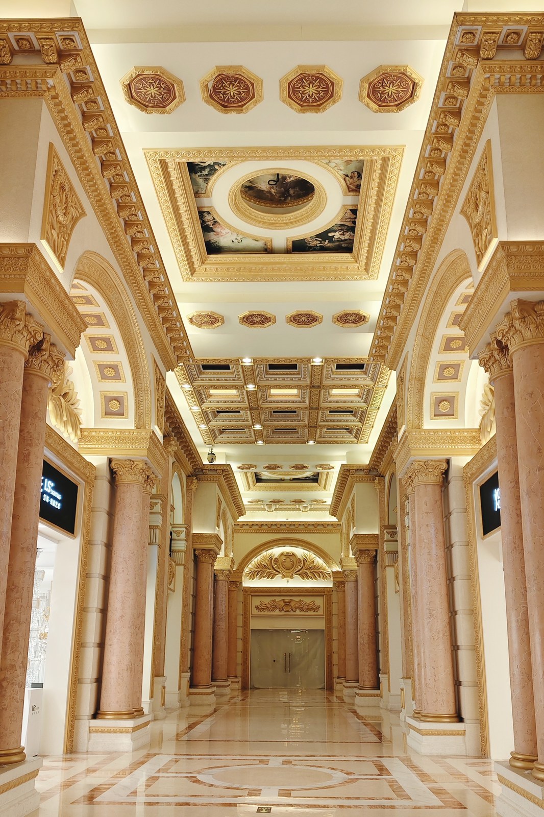 Ornate interior passage with paired columns, decorated ceiling panels and a reflective floor.