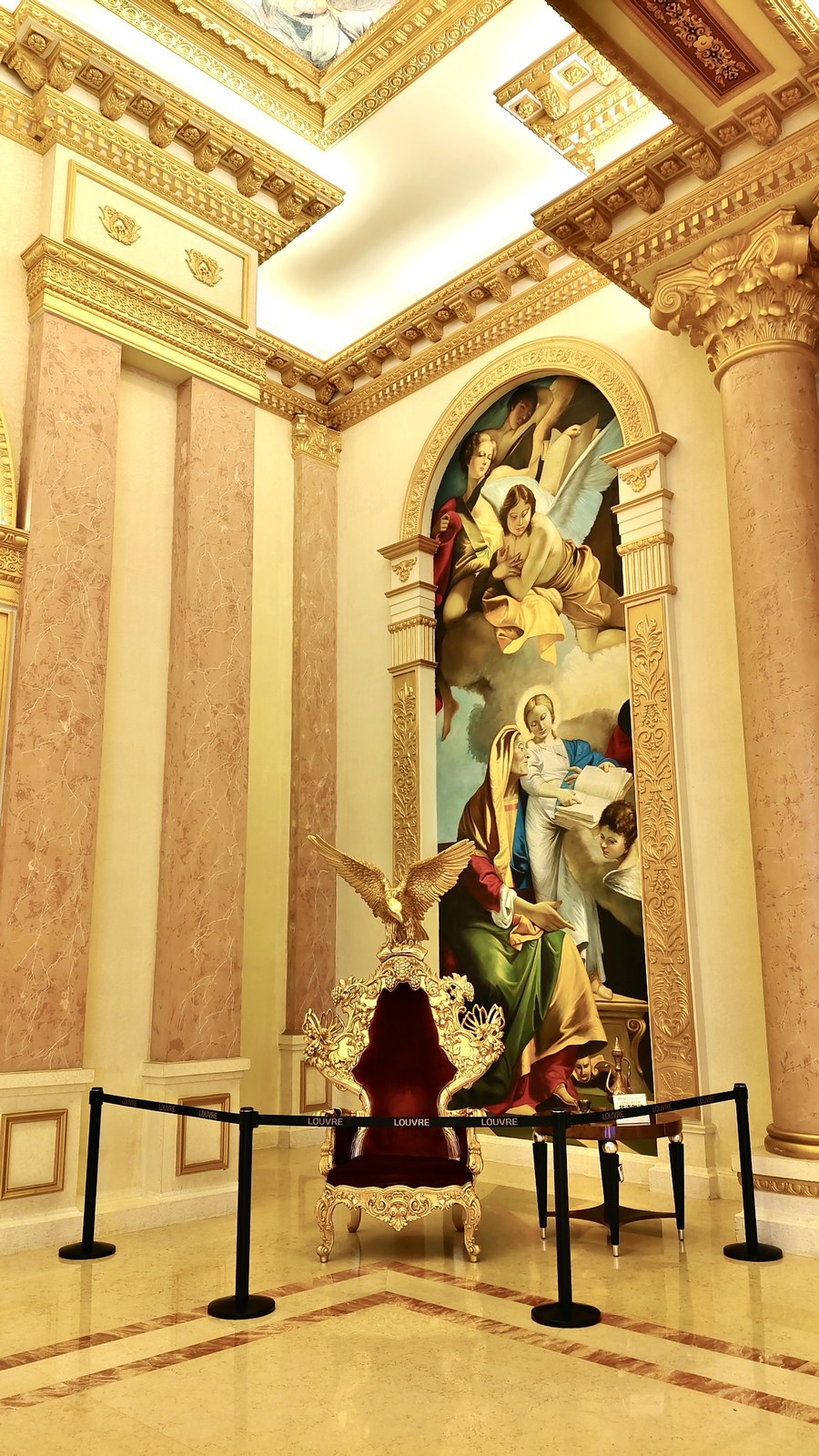 Roped-off ornate chair with an eagle-shaped crest in front of a large arched wall painting.