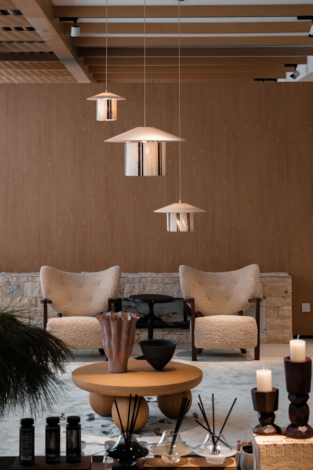Two cream lounge chairs against a wood wall, with a round table and three hanging lights.