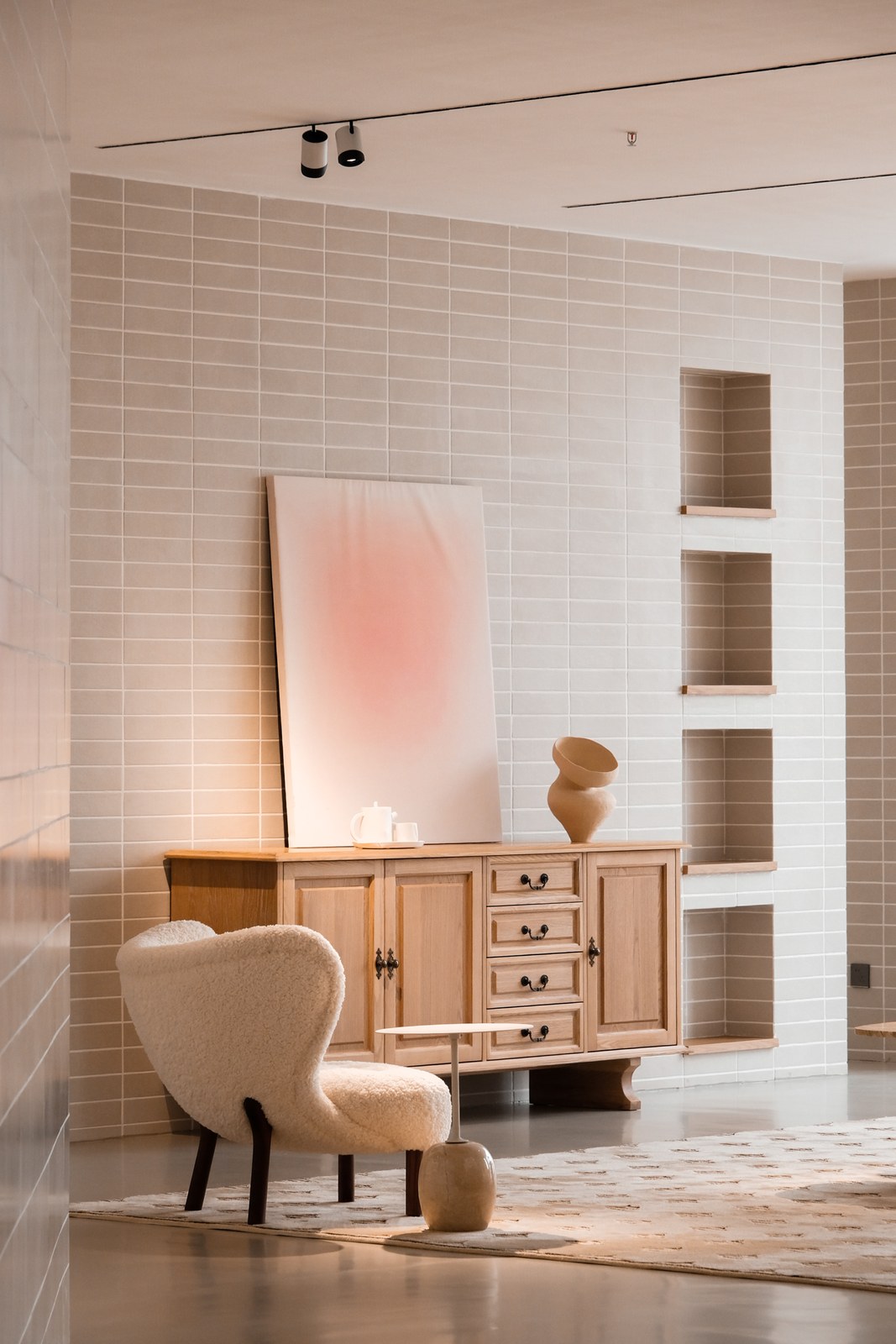 Pale wood-toned sideboard with an upholstered accent chair, abstract artwork and a sculptural vase.