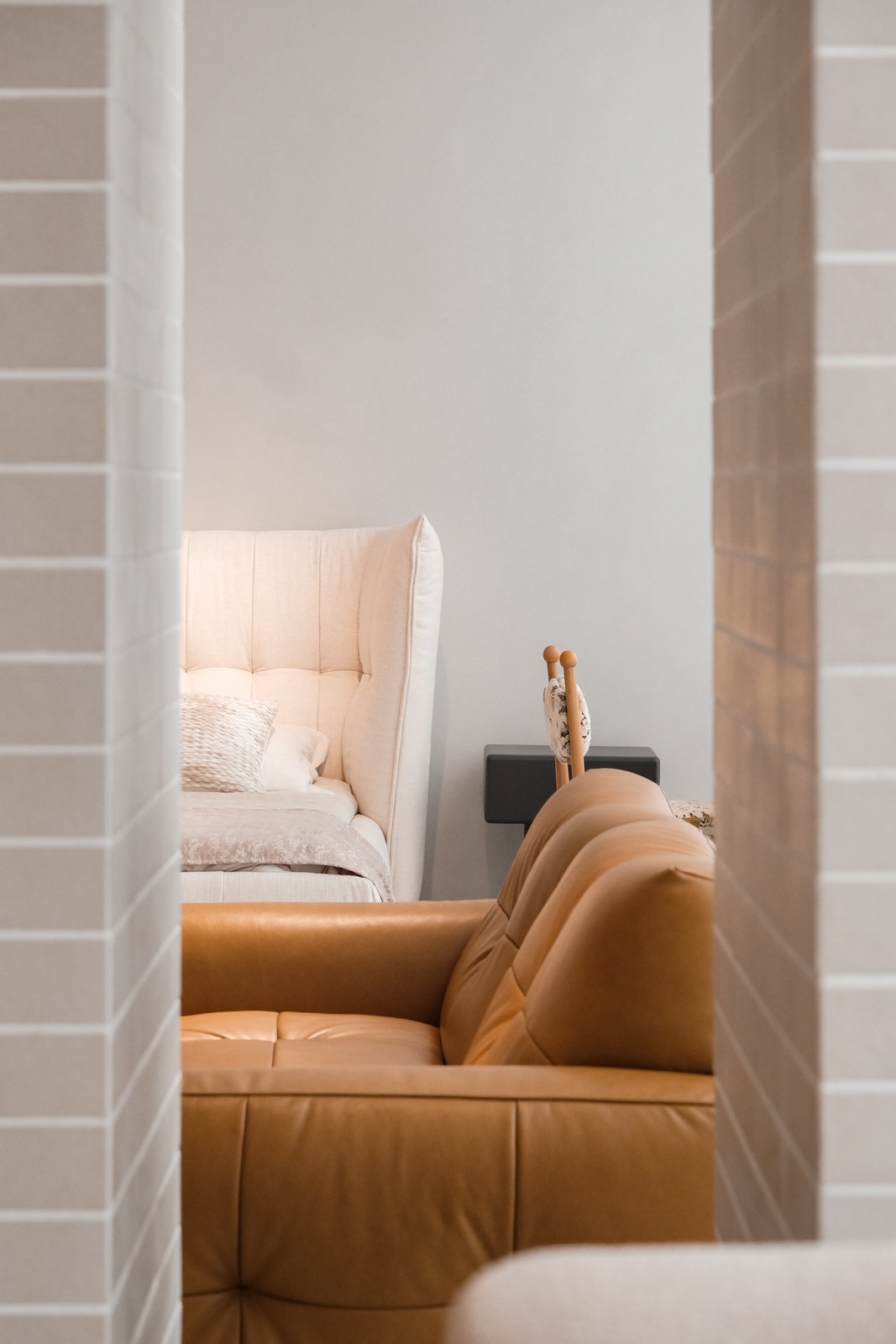 Caramel-toned sofa in the foreground with a pale padded bed behind a tiled doorway.