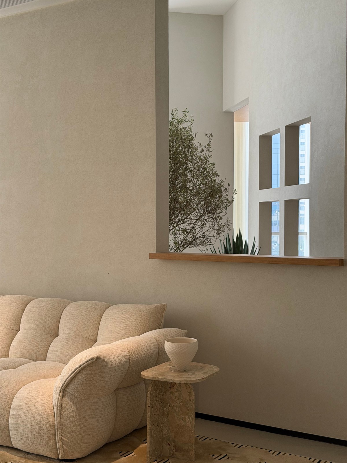 Cream upholstered sofa beside a pale veined side table, with greenery beyond a wall opening.