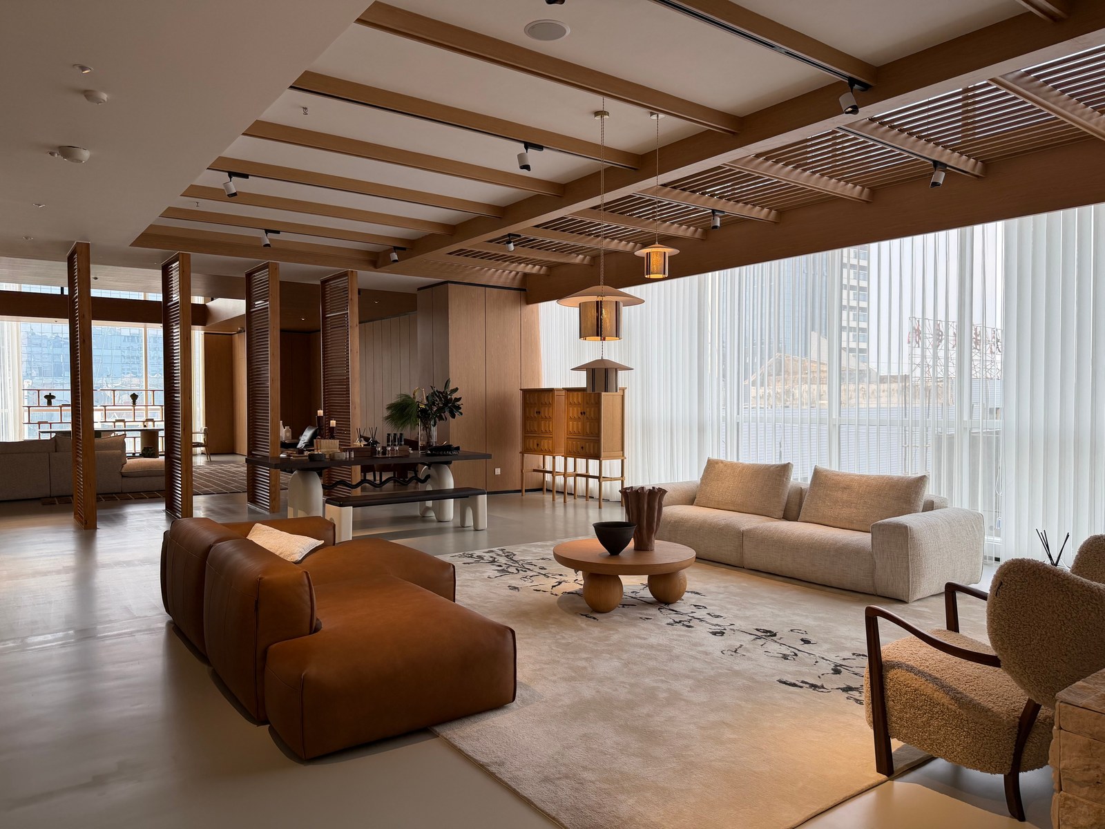 Caramel and cream sofas around a round table beneath timber-toned beams and pendant lights.
