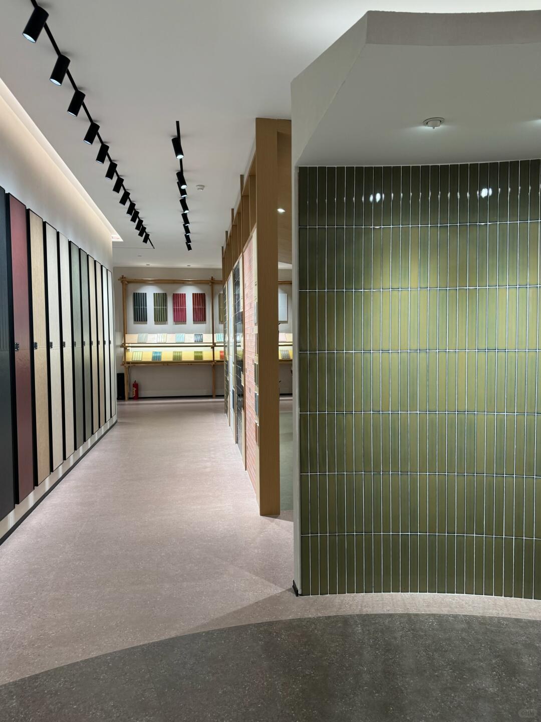 Olive-green vertically laid tiles on a curved partition beside full-height sample panels.