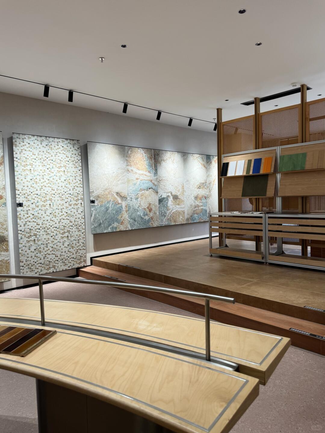 A mosaic panel and broad veined surface display behind open wooden sample stands.