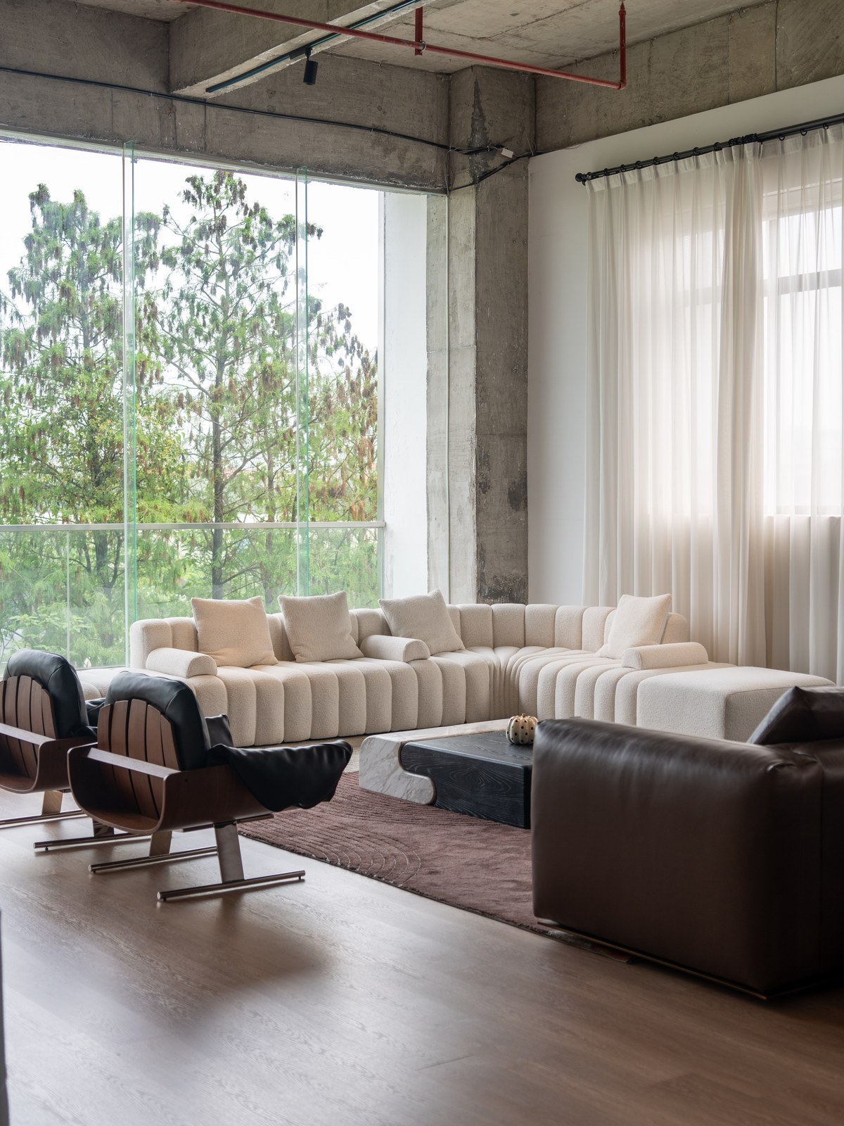 Cream corner sofa and dark lounge chairs in a daylit seating area with exposed concrete above.
