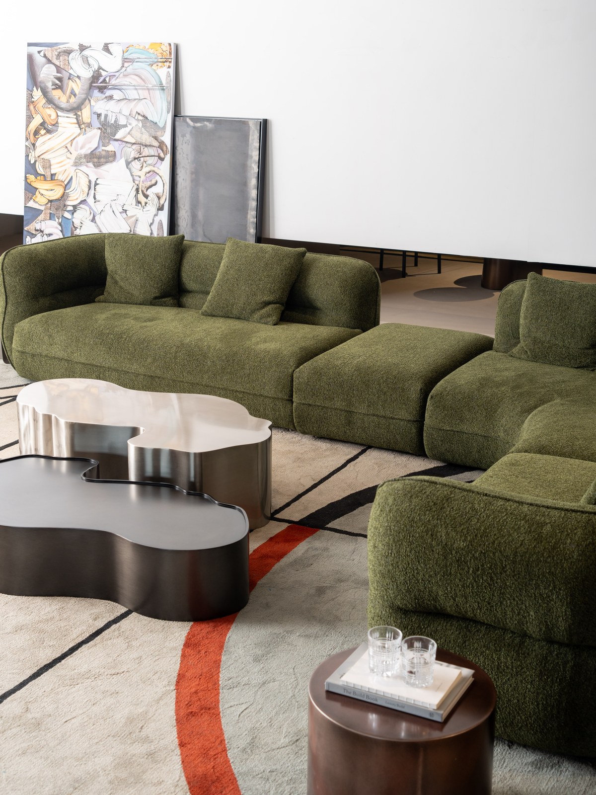 Close view of an olive-green modular sofa with rounded metal-finish coffee tables.