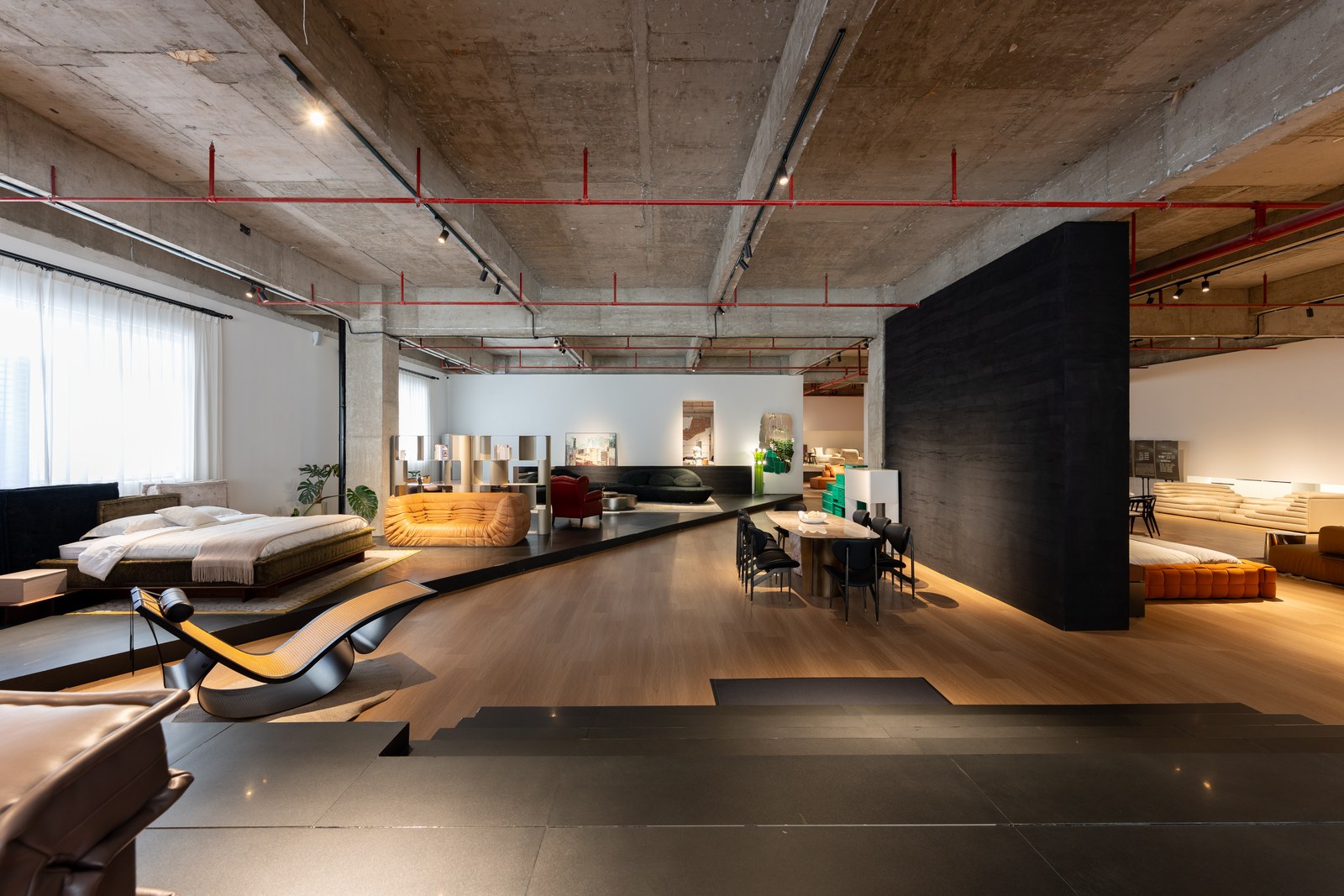 Open showroom containing bed displays, low sofas, dining furniture and a curved chaise.