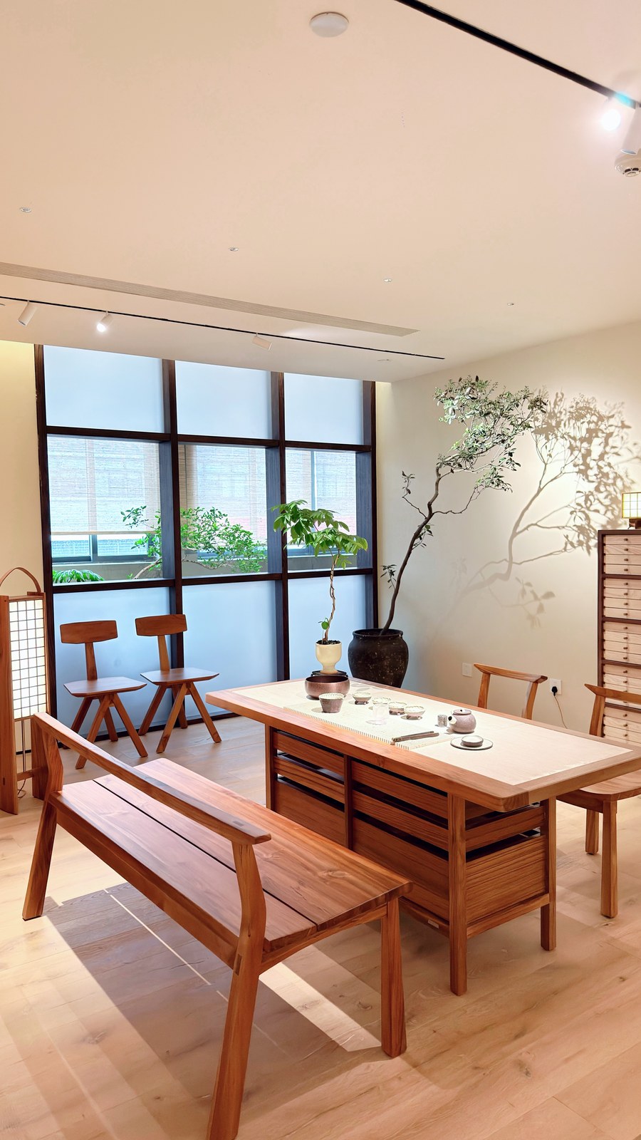 Wood-toned tea table with matching bench and chairs, ceramics and indoor plants.