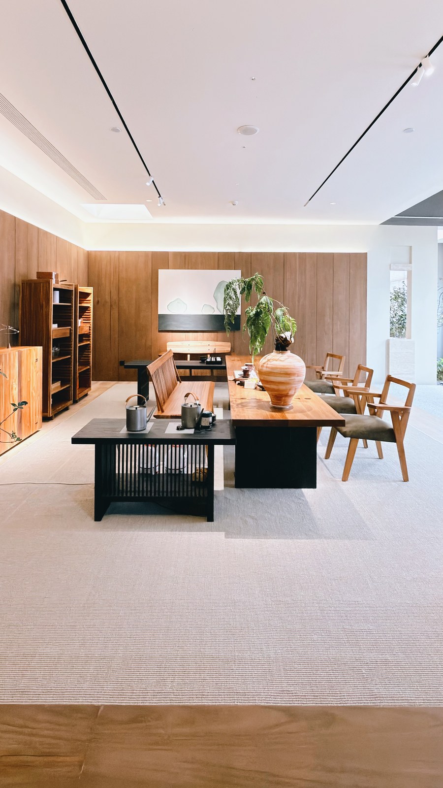 Long wood-toned table with bench and chairs, framed by cabinets and open shelving.