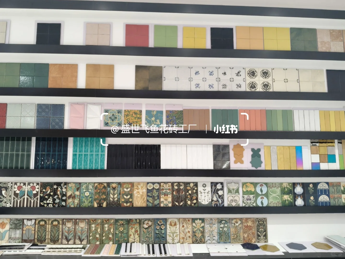 Horizontal display shelves holding colourful square tiles, slim glazed strips and botanical decorative tiles.