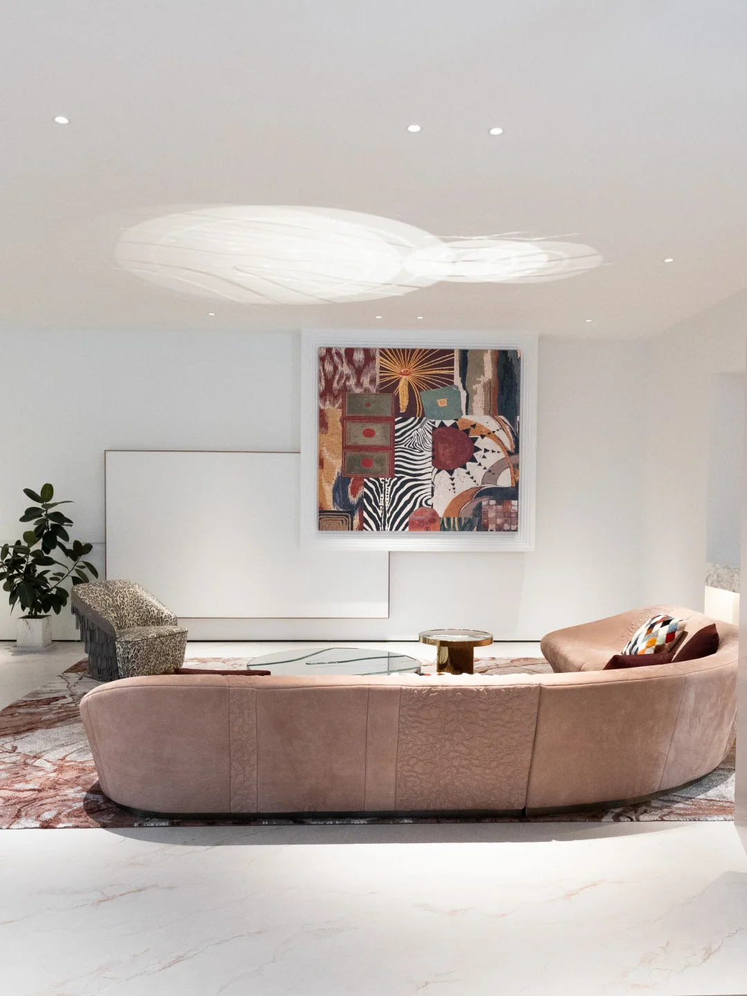 Blush curved sofa seen from behind, a patterned accent chair, glass coffee table and large abstract artwork in a bright showroom.