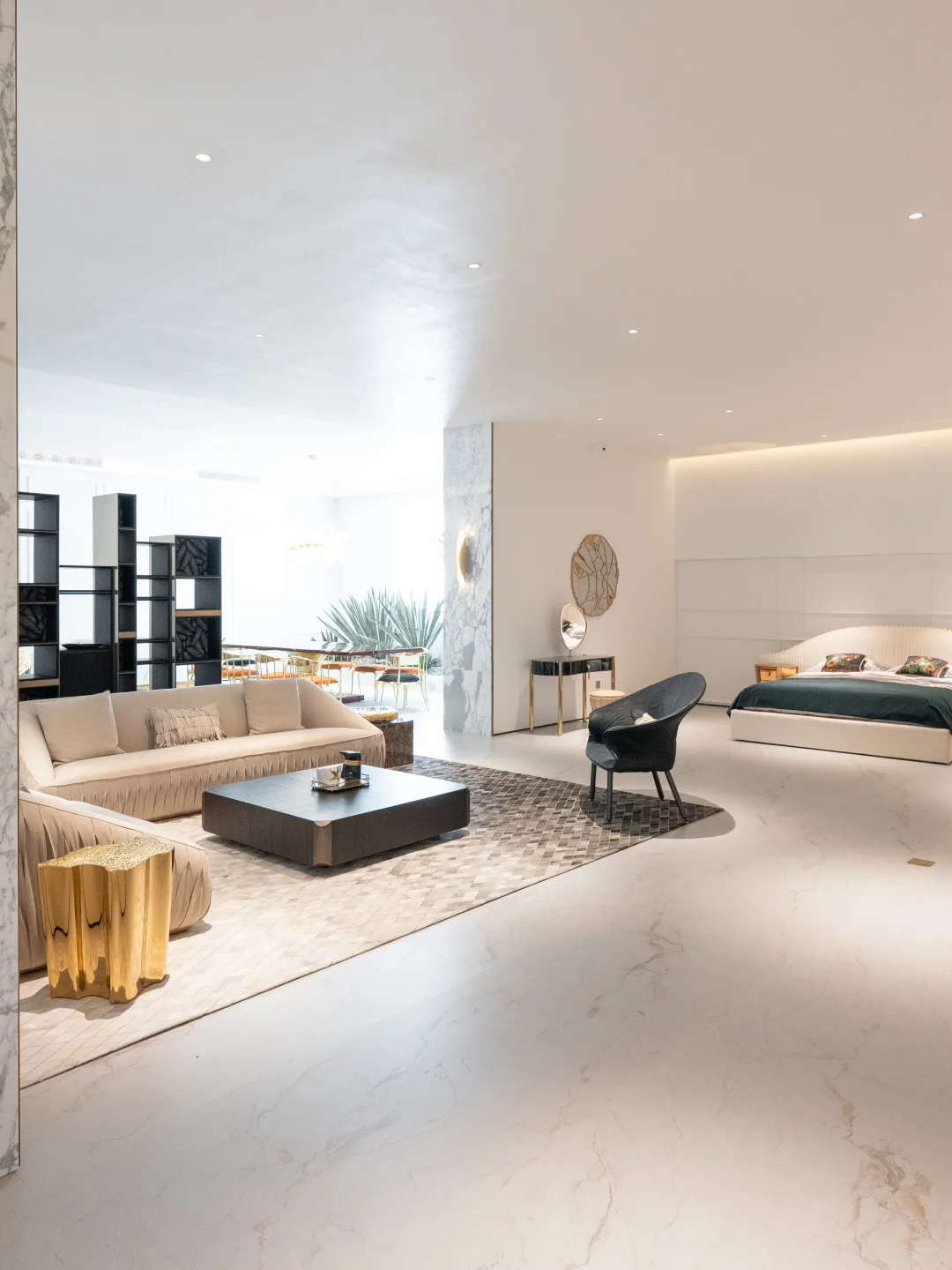 Cream sofas and a black accent chair around a low dark table, with a cream bed and green bedcover displayed in the adjoining room.