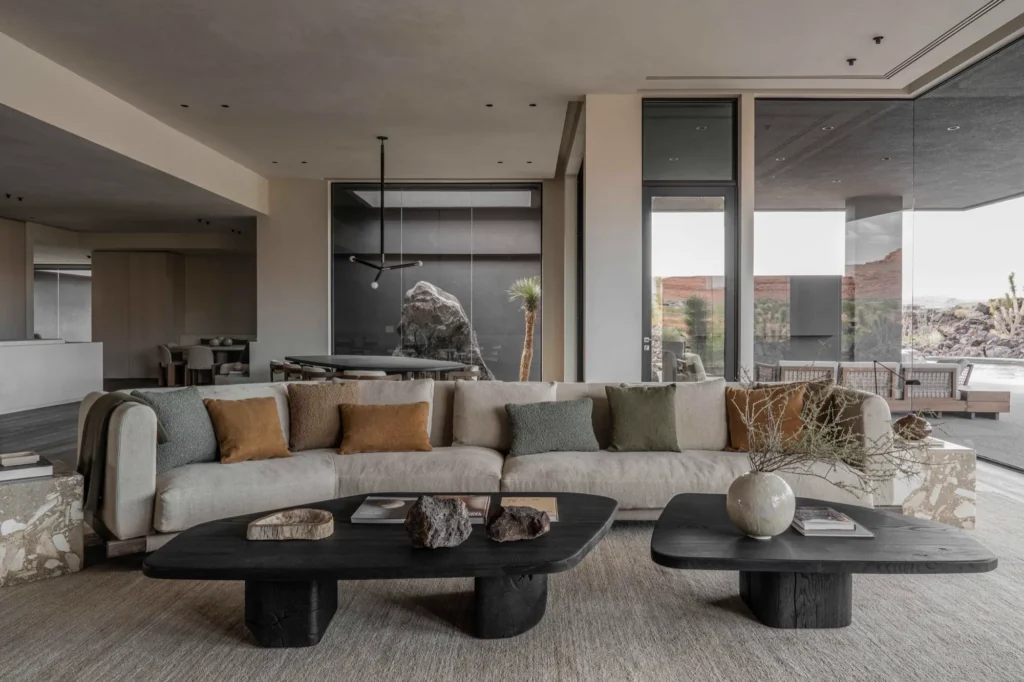 Contemporary lounge with a large cream sectional sofa and black stone coffee tables in a glass-walled room