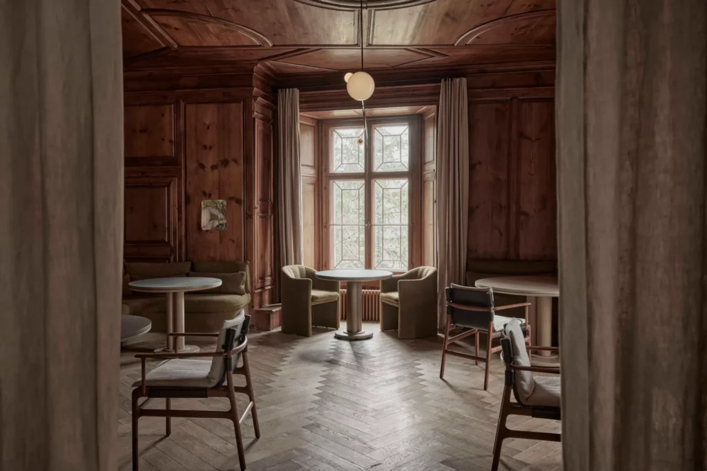 Wood-panelled private dining room with round tables, upholstered chairs and floor-length curtains
