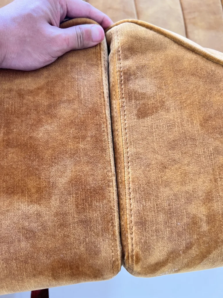 Hand checking the stitched corner seam of a tan leather sofa during inspection