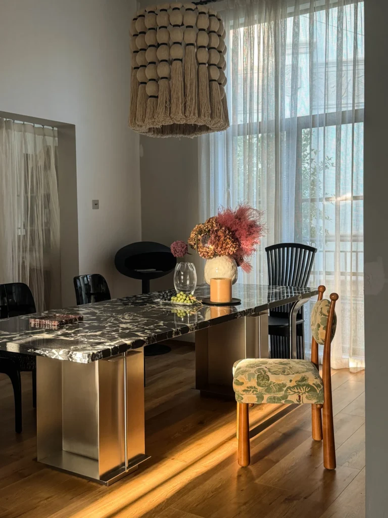Dining room with a dark stone table, patterned upholstered chairs and a pendant light