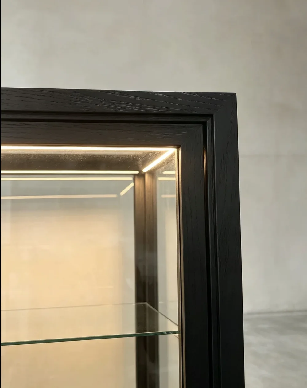 Detail of a black wood and glass display cabinet with concealed warm LED lighting