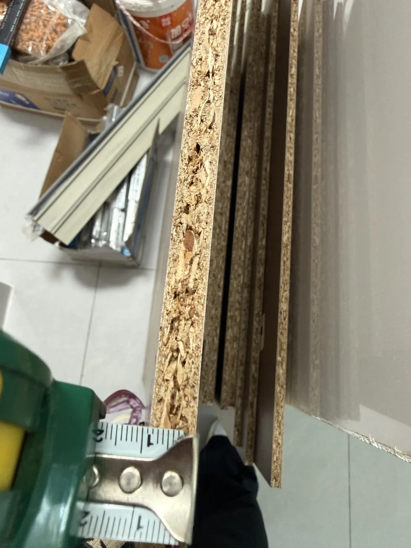 A tape measure on the raw edge of a particleboard panel, showing the chip core and the 18 mm thickness the buyer's contract specified.
