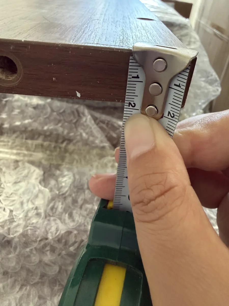 Measuring panel thickness with a tape measure at the board edge; the buyer checked every carcass panel against the 18 mm in her contract.