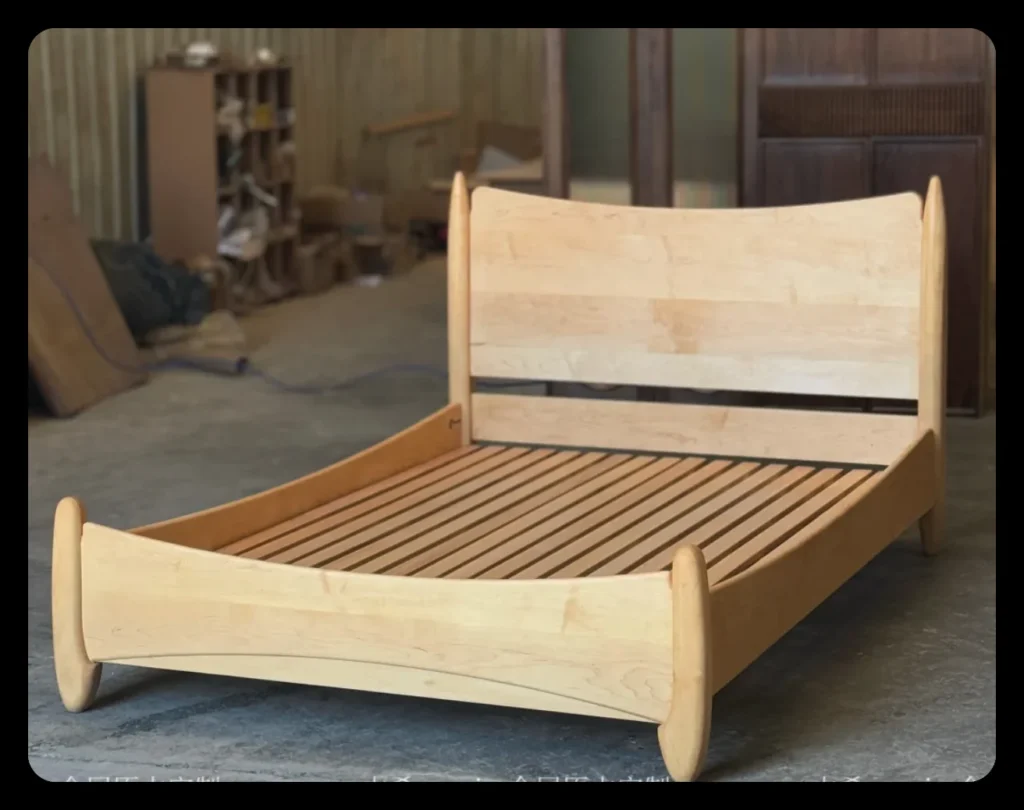 Solid maple bed frame standing in a workshop before finishing