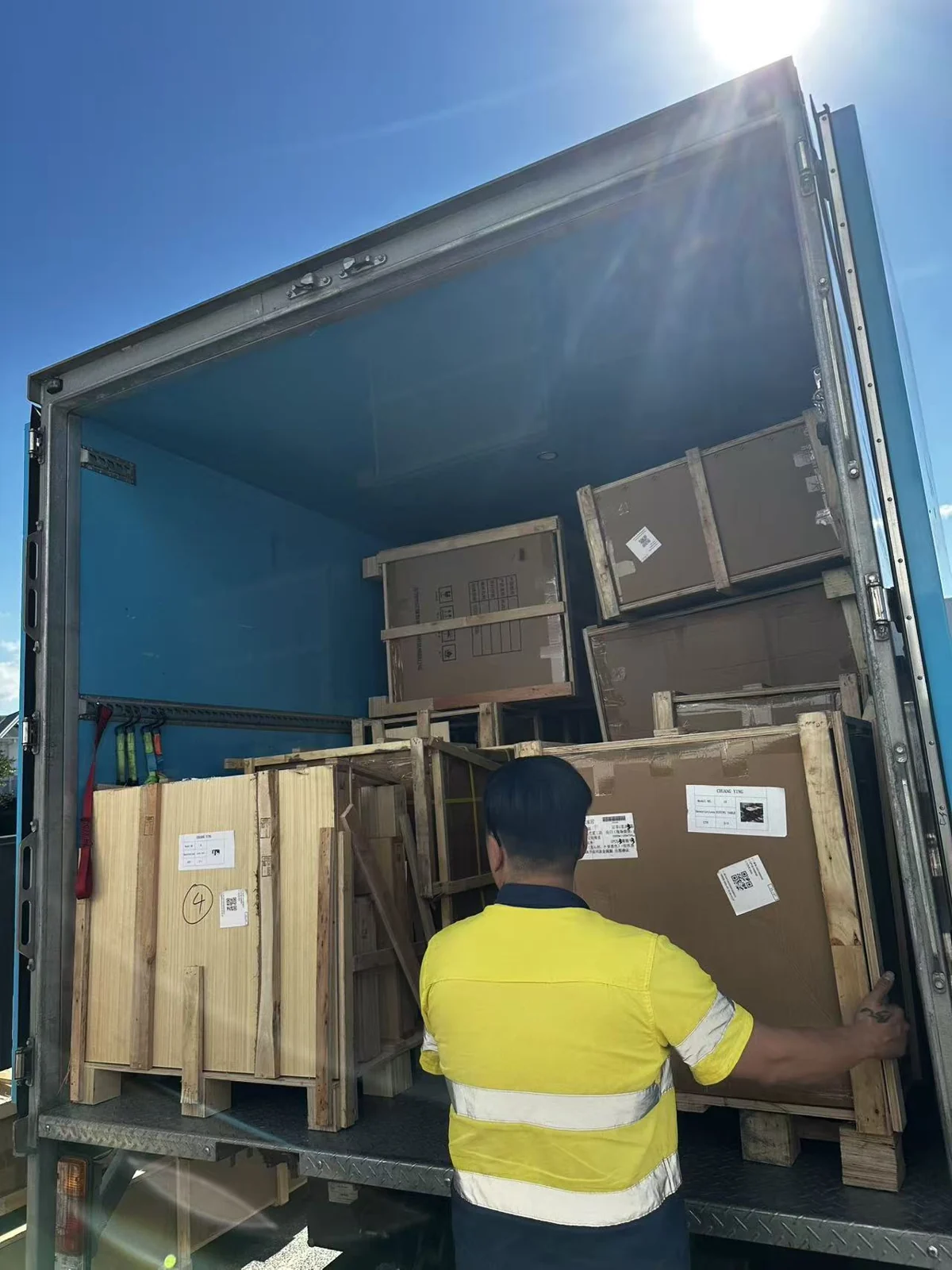 A delivery crew member handling a timber-framed crate at the rear of the truck
