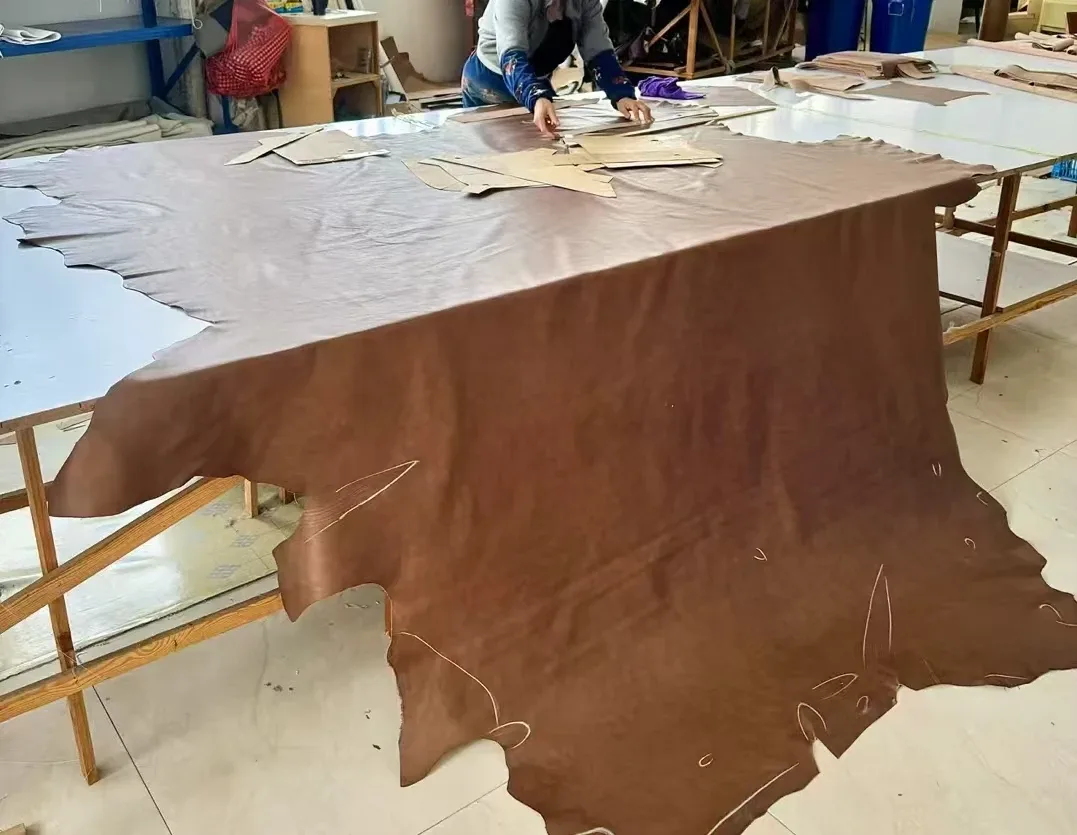 A whole leather hide laid out with cutting templates in the same Foshan sofa workshop. On a live call, ask how many hides your sofa needs and where.