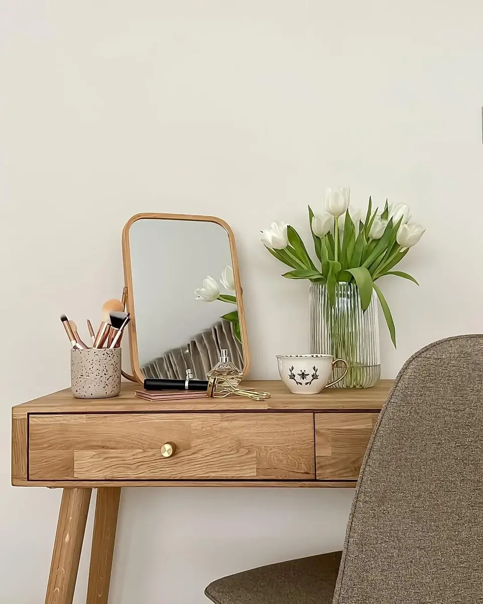 Wood-finish desk with a light upholstered chair and vase of flowers