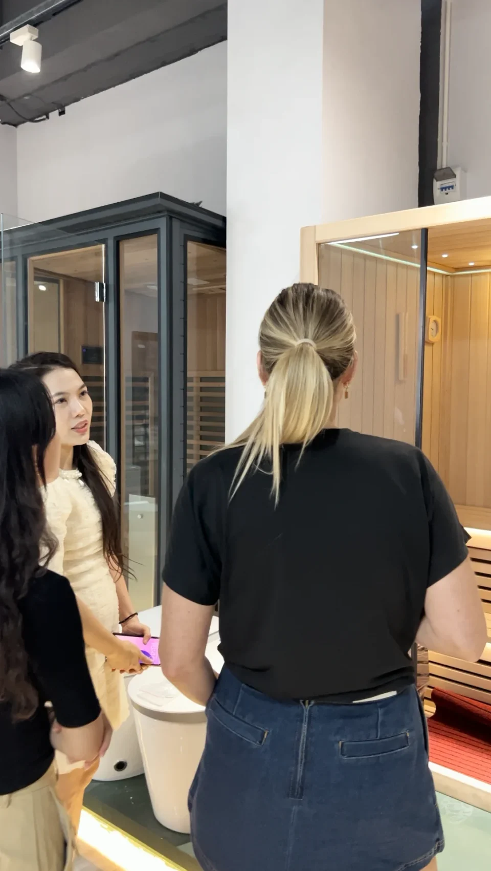 A buyer and guide standing beside display sauna cabins in a bathroom showroom.