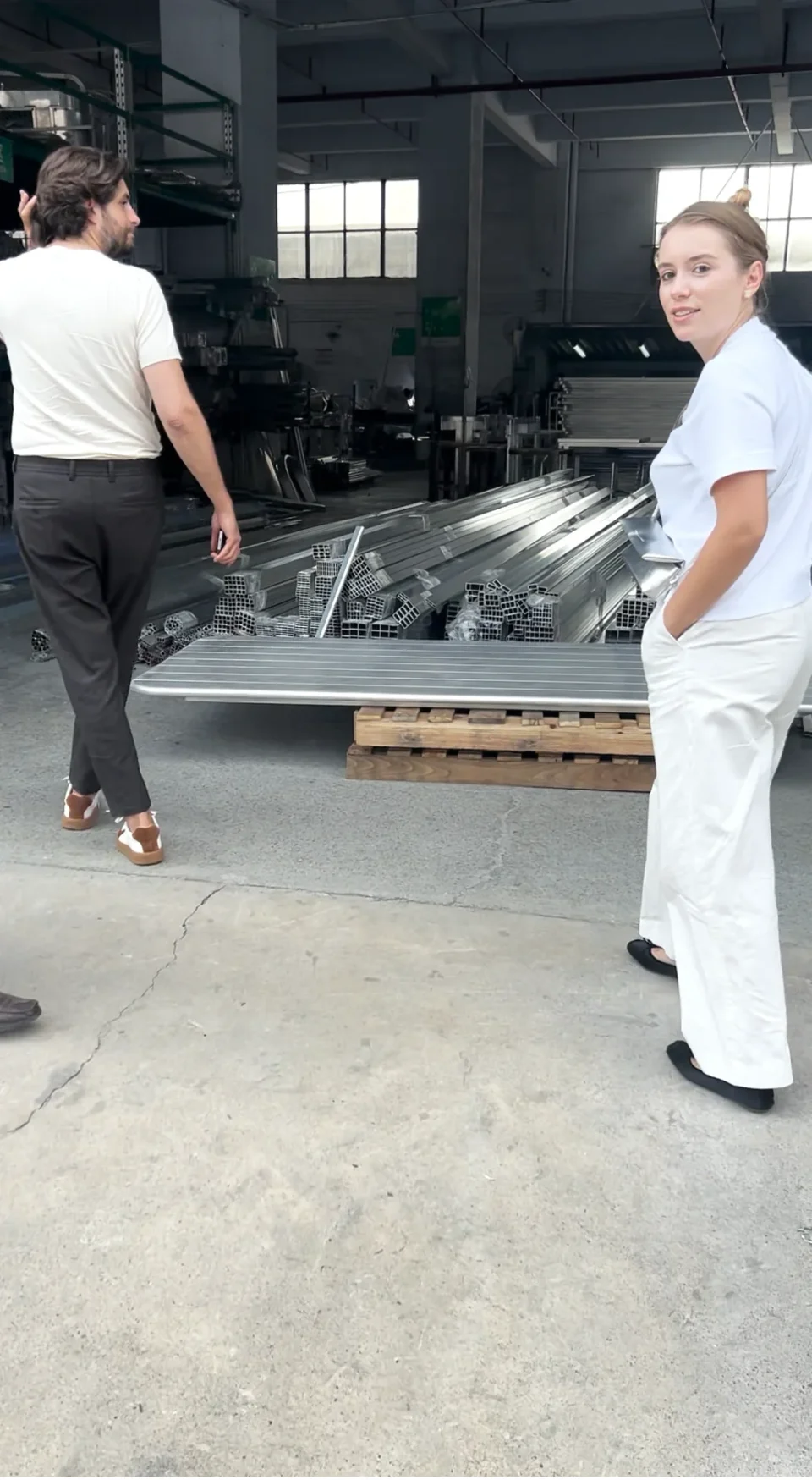 Visitors walking beside metal components in a furniture production space.