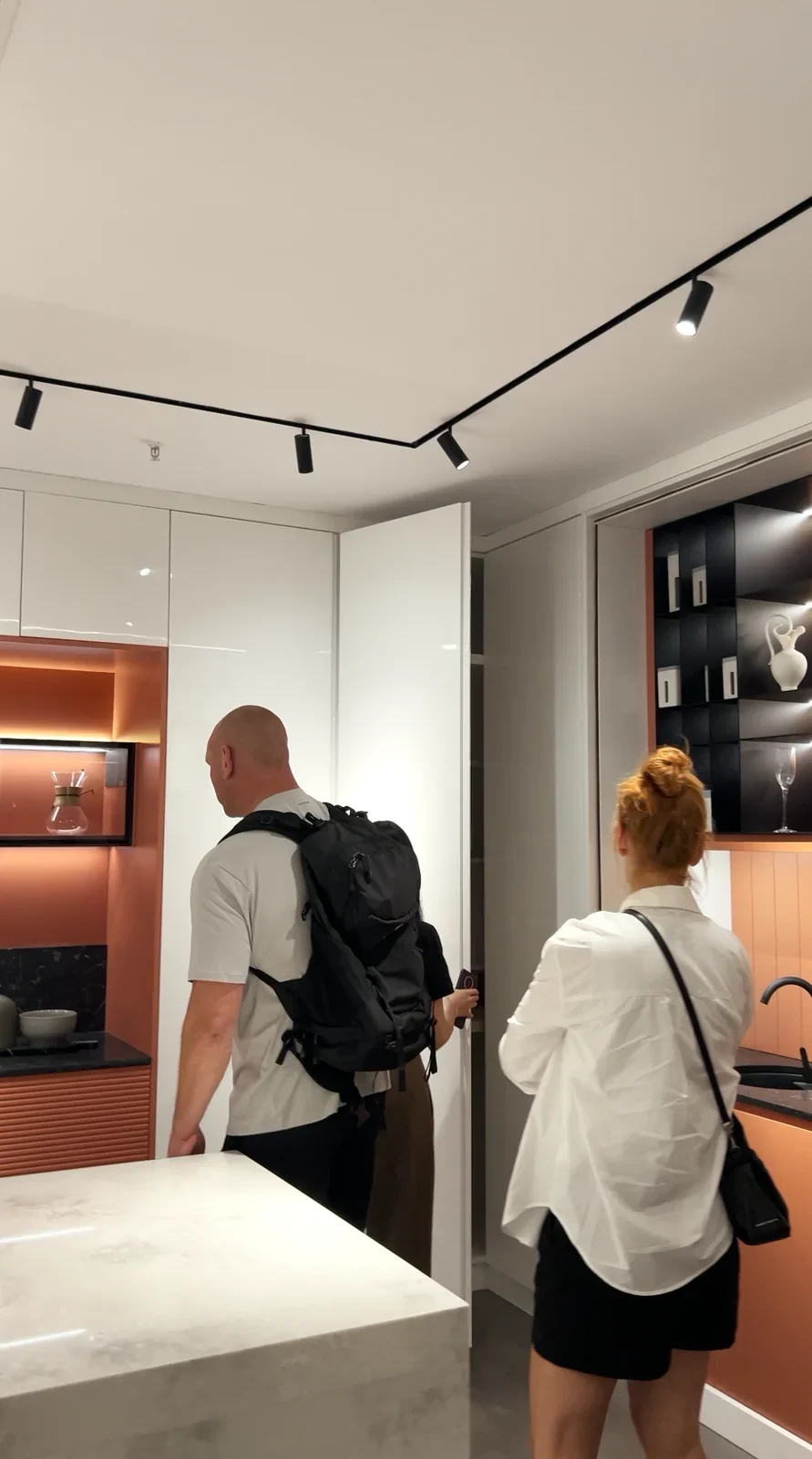 Visitors walking past a kitchen island and cabinet displays in a showroom.