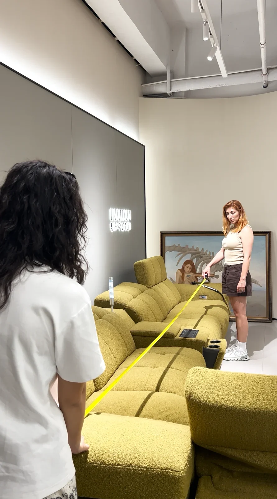 A tape measure stretched along a green sectional sofa in a furniture showroom.